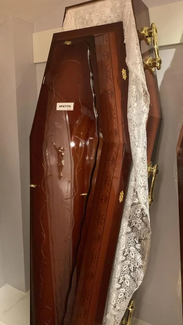 Urna funerária Apatita em acabamento escuro com figura religiosa aplicada na tampa.