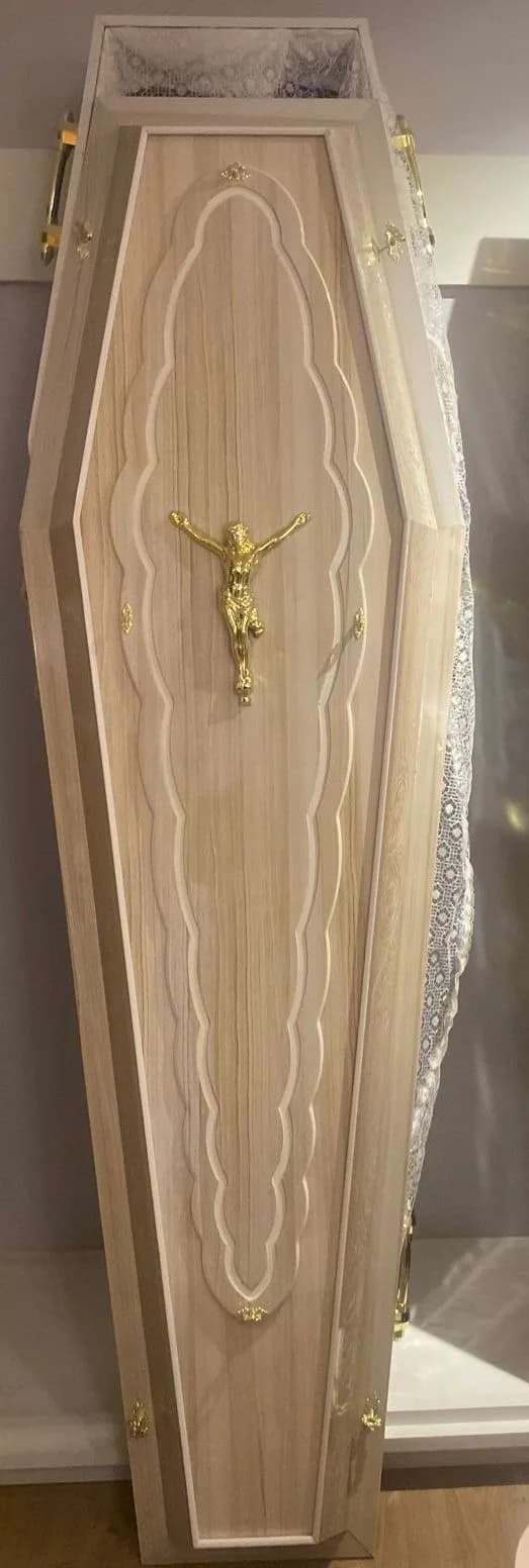 Urna funerária clara em tom champanhe com figura religiosa dourada.